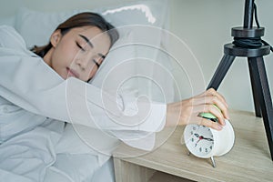 Asian beautiful tired young woman turn off an alarm clock in morning. Attractive sleeping girl in pajamas feel lazy and sick to