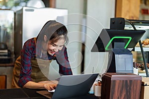 Asian beautiful woman cafe owner Checking orders from customers who ordered cakes and bread. Via online shopping with laptop