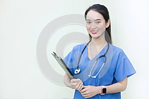 Asian beautiful  woman doctor standing smiling in a blue lab shirt, holding patient documents in hand.