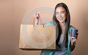 Asian beautiful woman holding cup of coffee, shopping paper bag, presenting environmental sustainable packages, smiling with