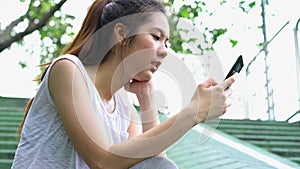 Asian beautiful woman holding smartphone after exercise in summer at outdoors. Teenages athlete girl sitting on stairs and happy w