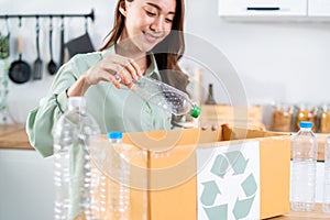 Asian beautiful woman separating trash for further recycling at home. Attractive female put plastic bottles into recycle box for