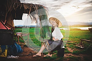 Asian Beautiful woman in Thai local dress sitting and working with fishing net in fishing village with field and lake