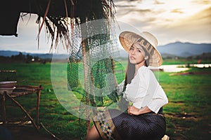 Asian Beautiful woman in Thai local dress sitting and working with fishing net in fishing village with field and lake