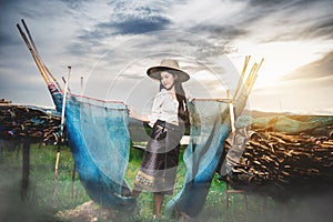Asian Beautiful woman in Thai local dress standing and working with fishing net in fishing village with field and lake