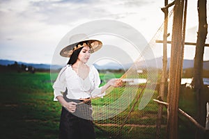 Asian Beautiful woman in Thai local dress working with fishing net in fishing village with field and lake background