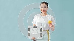 Asian beautiful woman are using the measuring tape to measure around the waist and holding  weight scale on blue background