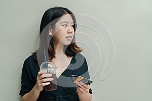 Asian beautiful woman Wearing a black shirt, standing drinking cold coffee in the hand And have a credit card in hand Happy face