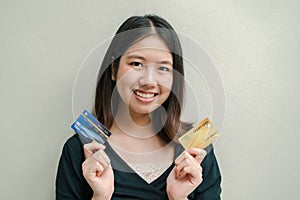 Asian beautiful woman Wearing a black shirt There are credit cards in both hands. Happy face Standing in the gray wall