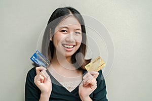 Asian beautiful woman Wearing a black shirt There are credit cards in both hands. Happy face Standing in the gray wall