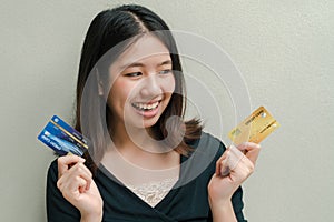 Asian beautiful woman Wearing a black shirt There are credit cards in both hands. Happy face Standing in the gray wall