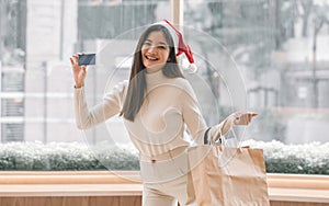 Asian woman wearing santa hat, holding credit card and paper bags