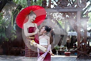 Asian beautiful woman wear a luxury national costume and holding a red umbrella and a little girl standing in classic thai house