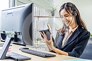 Asian beautiful young girl call center operator in headset answering calls and using tablet at call center