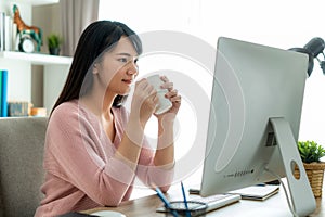Asian beautiful young woman work from home working on computer and drinking coffee while working in living room at home. Social