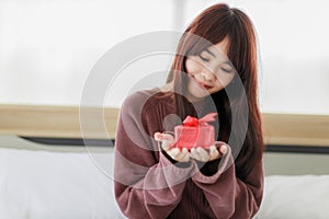 Asian beautifull woman holding red gift box and happiness in her bed room. Stay at home