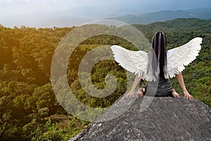 Asian beauty woman with bird wings at the back, sitting on the rocks in the mountains.