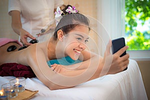 Asian beauty woman lying down on massage bed with traditional hot stones along the spine at Thai spa and wellness center. She tak