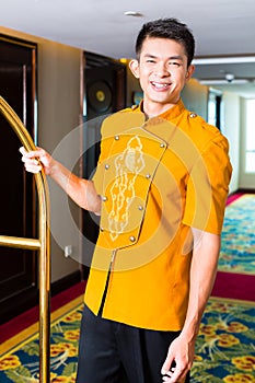 Asian bell boy or porter bringing suitcase to hotel room