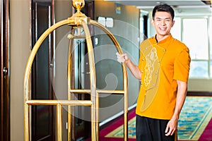 Asian bell boy or porter bringing suitcase to hotel room