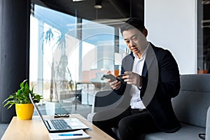 Asian boss businessman makes online shopping sitting in the office, thoughtful makes a choice in the online store