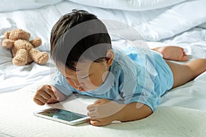 Asian boy about 2 years old, watching and playing mobile phone on the white bed