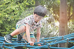 Asian boy climbing on rope bridge in playground