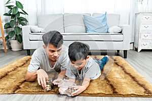 Asian boy in clothes sitting on the floor, in front of him is a table with a piggy bank. boy took the coin in his father\'s