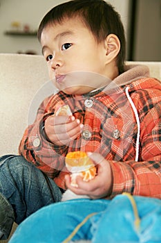 Asian boy eating orange on sofa