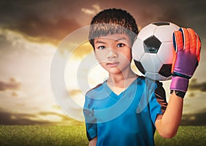 Asian boy is football goalkeeper wearing gloves and holding a soccer ball with cloud sky background