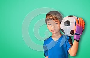 Asian boy is football goalkeeper wearing gloves and holding a soccer ball on green background copy space