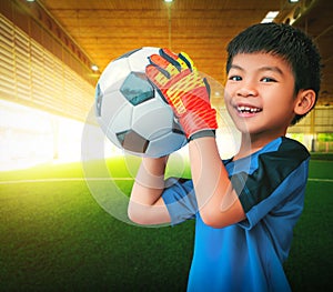 Asian boy a football goalkeeper wearing gloves and holding a soccer ball for youth sport concept