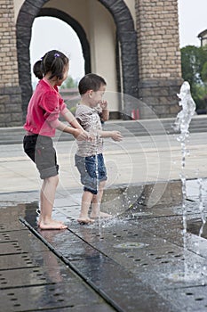 Asian boy and girl play by fountain