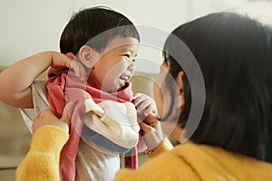 Asian Boy having fun while mother helping to get dressed