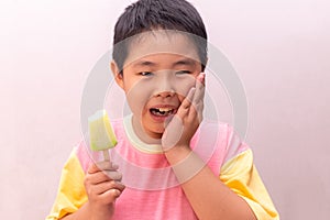 Asian boy with hypersensitive teeth eating eating a colorful frozen popsicle in the summer