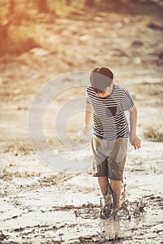 Asian boy jumping in mud pool of water at the summer or autumn d