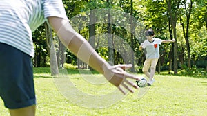 Asian boy kicking soccer toward his father as goal keeper outdoors in summer in slow motion