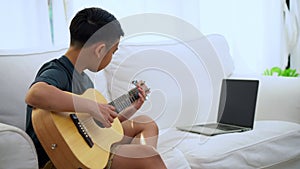 Asian boy learning to play the guitar in virtual meeting for play music online together with friend or teacher in video conference