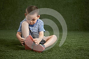 Asian boy learns to tying shoelaces on green grass background