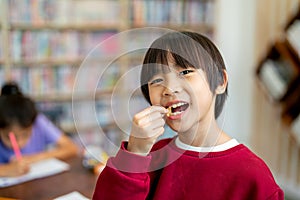 Asian boy look like Chinese enjoy with eating candy in classroom while his friend concentrate in drawing or painting work