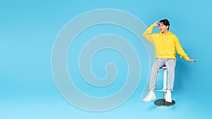 Asian Boy Looking Aside Holding Hand At Forehead, Blue Background