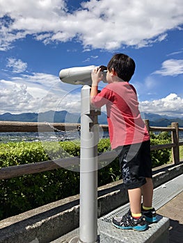 Asian boy looking through telescope with blue sky background