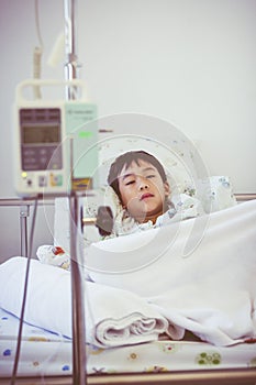 Asian boy lying on sickbed with infusion pump intravenous IV drip. Retro style.