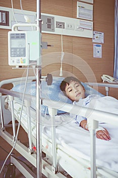 Asian boy lying on sickbed with infusion pump intravenous IV drip. Retro style.