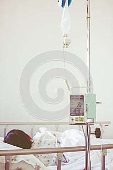 Asian boy lying on sickbed with infusion pump intravenous IV drip. Vintage style.