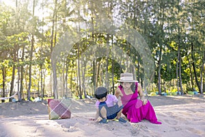 Asian boy and mom woman relaxing on tropical beach, they are njoy freedom and fresh air, wearing stylish hat and clothes. Happy