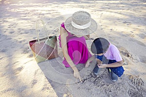 Asian boy and mom woman relaxing on tropical beach, they are njoy freedom and fresh air, wearing stylish hat and clothes. Happy