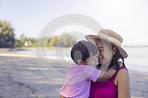 Asian boy and mom woman relaxing on tropical beach, they are njoy freedom and fresh air, wearing stylish hat and clothes. Happy