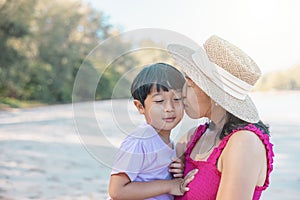 Asian boy and mom woman relaxing on tropical beach, they are njoy freedom and fresh air, wearing stylish hat and clothes. Happy