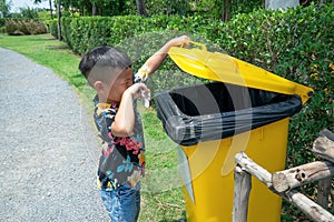 Asian boy is open yellow trash with his left hand and his right hand is holding garbage. Big bin is very bad smell.